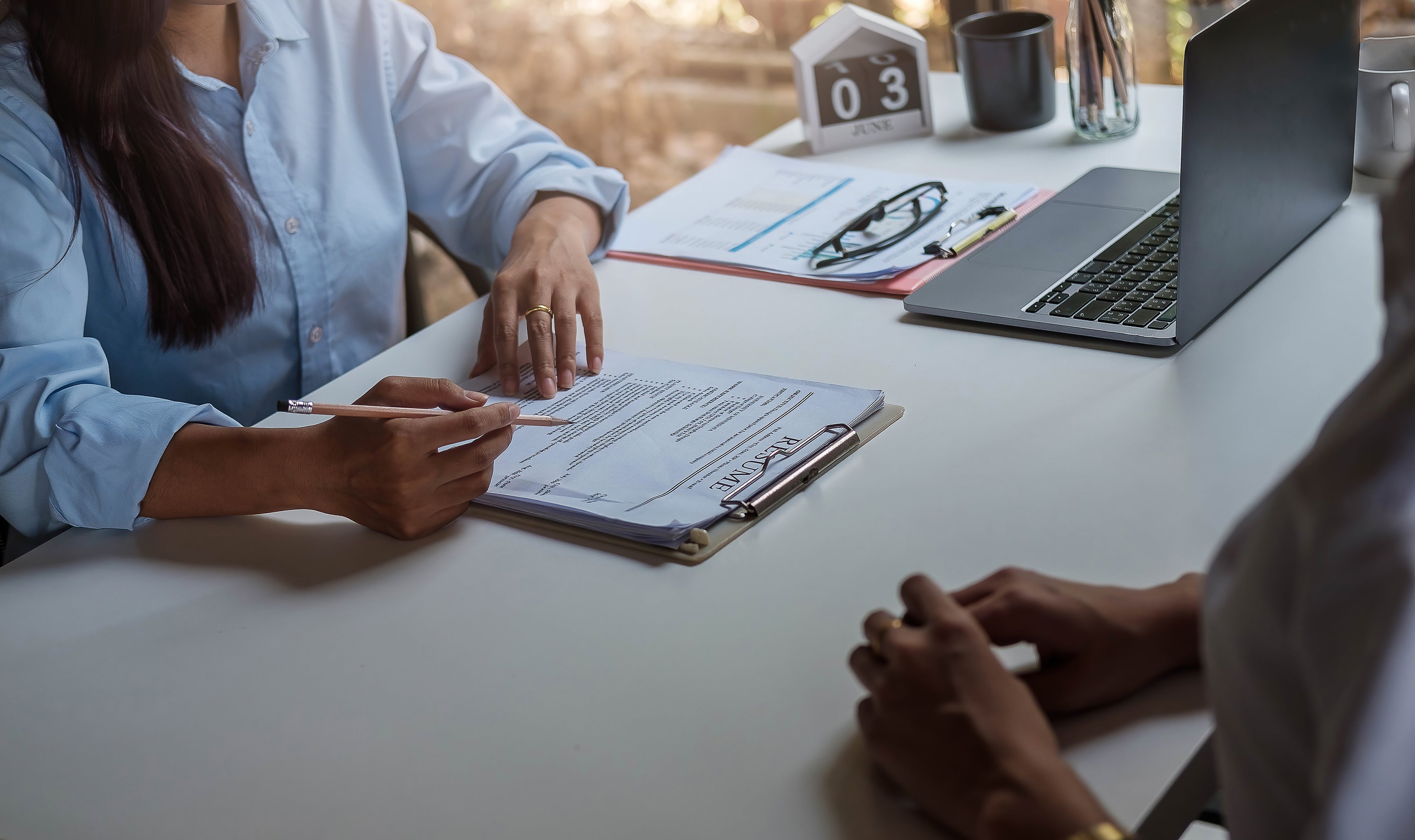 Photo of two people on either side of a table during an interview. It is cropped to only show hands